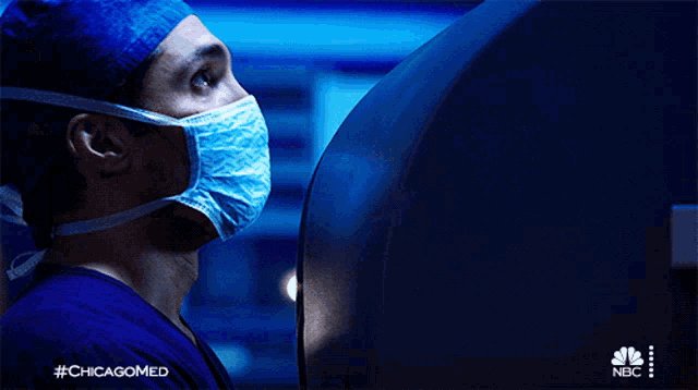 a man wearing a mask and a surgical cap is looking at a computer screen with #chicagomed written on the bottom