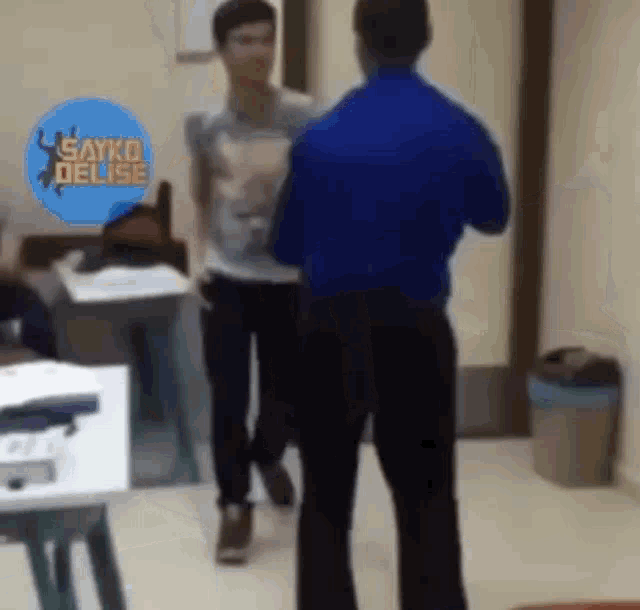 two men are standing next to each other in a room and talking to each other .