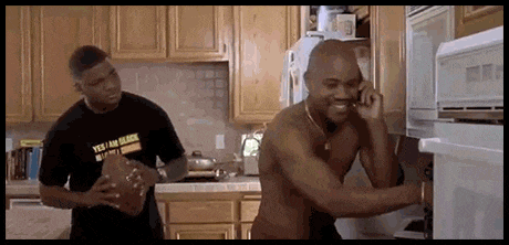 a shirtless man is talking on a cell phone while another man holds a football .