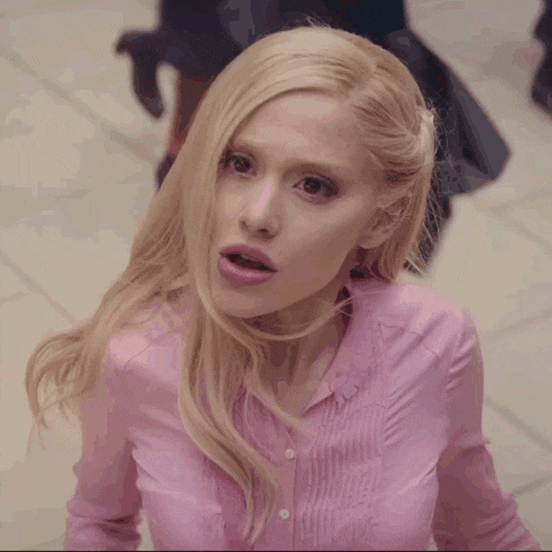 a woman with blonde hair and a pink shirt looks surprised