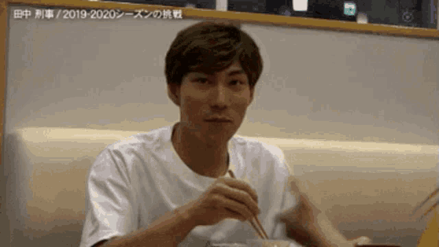a man in a white shirt is eating with chopsticks in a restaurant .