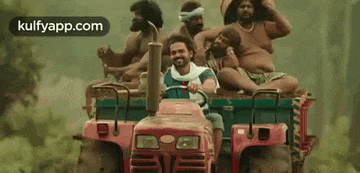 a group of men are riding on the back of a tractor in the woods .