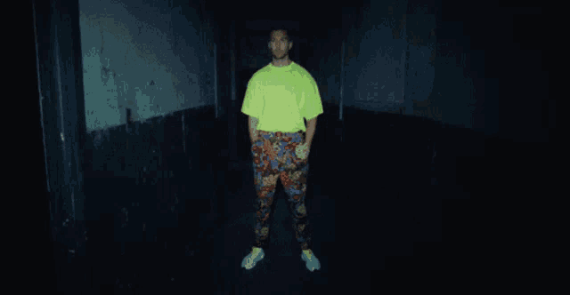 a man wearing a neon yellow shirt and colorful pants is standing in a dark room