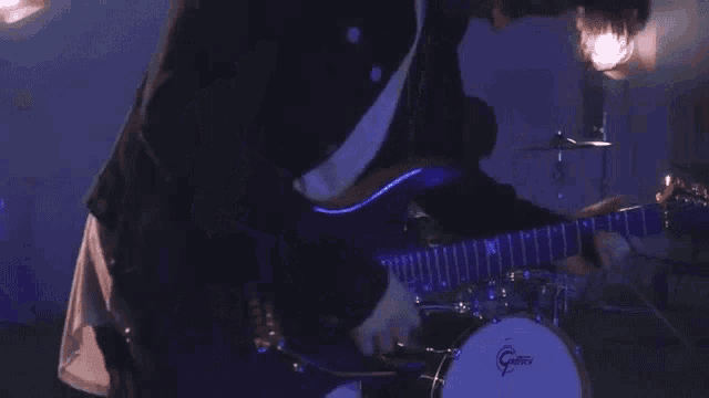 a man is playing a guitar and a drum set in a dark room .