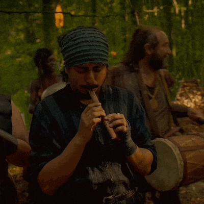 a man wearing a headband plays a flute in the woods