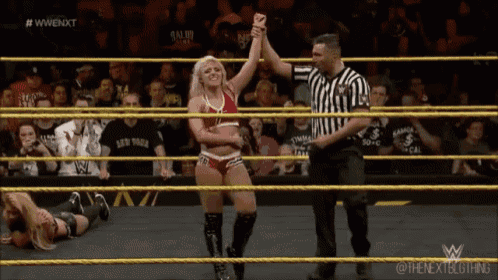 a female wrestler is being congratulated by a referee during a wrestling match