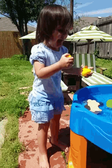 a little girl in a blue dress is playing with water toys