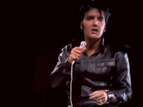 elvis presley is holding a microphone in his hand and singing into it .