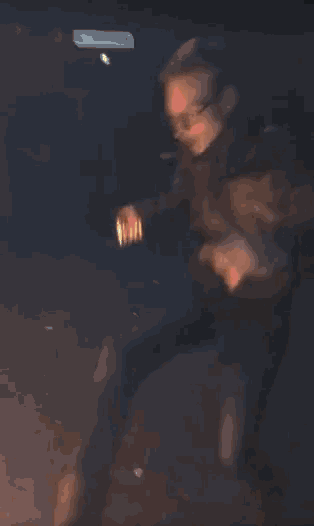 a blurry picture of a person standing in front of a fire with a bottle in their hand