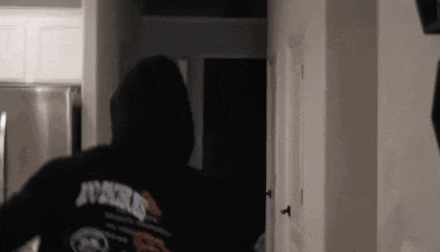 a man in a black hoodie is walking through a hallway .