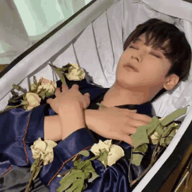 a young man is laying in a coffin with roses around his neck and chest .
