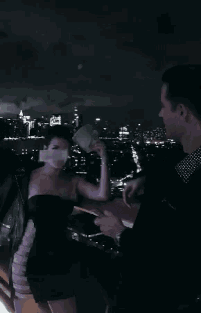a woman in a black dress is taking a picture of a city at night