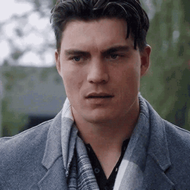 a man wearing a gray coat and a scarf is looking at the camera .