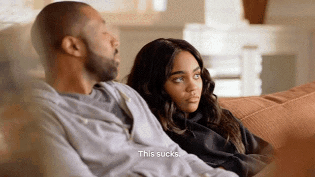 a man and a woman are sitting on a couch and the man says this sucks