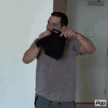 a man wearing a gray shirt and blue pants is holding a black shirt over his face .
