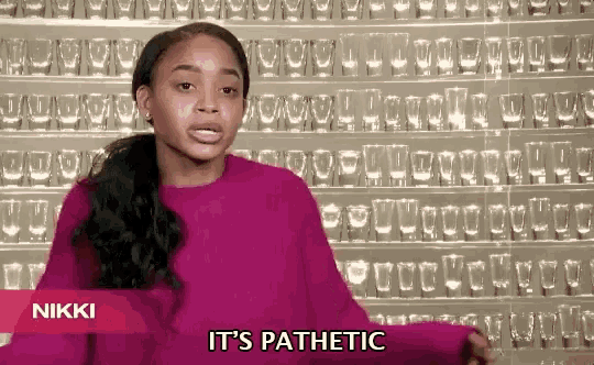 a woman says it 's pathetic in front of a wall of wine glasses
