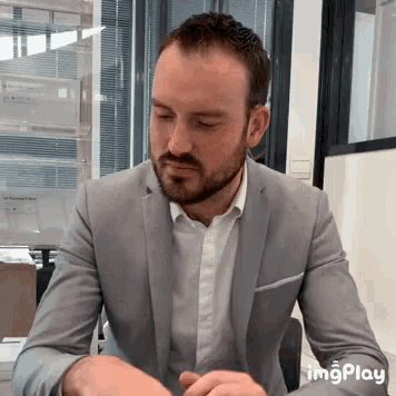 a man in a suit and white shirt is sitting at a desk with his eyes closed and the word imgplay visible