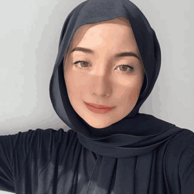 a woman wearing a black hijab and a black shirt smiles for the camera