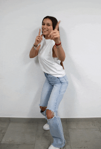 a woman wearing ripped jeans and a white tank top is giving the thumbs up sign