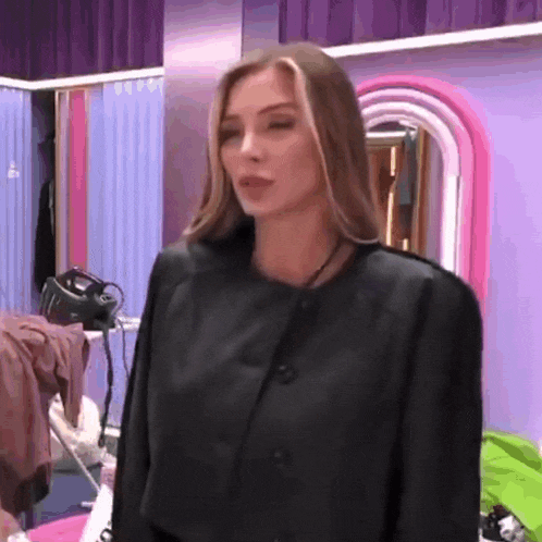 a woman in a black jacket is standing in front of a purple wall in a room .