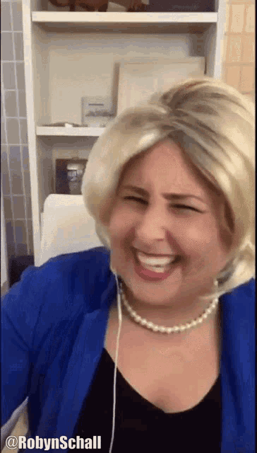 a woman wearing a wig and a pearl necklace is smiling and has the name robyn schall on the bottom right