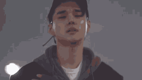 a young man wearing a hat and a hoodie is looking at the camera with his eyes closed .