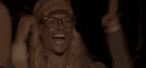 a woman wearing glasses and a headband is laughing and holding her head .