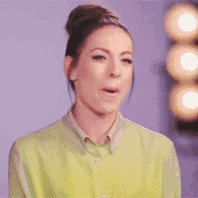 a woman wearing a green shirt and a bun is making a face .