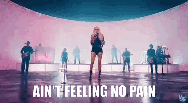 a woman is singing into a microphone with a band behind her and the words ain 't feeling no pain
