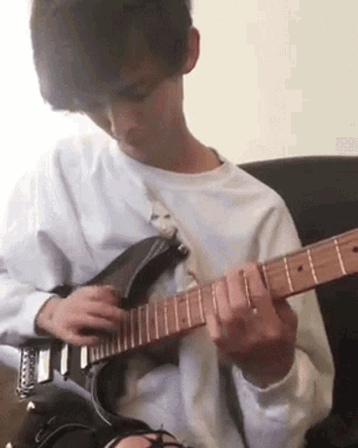a young man is sitting on a couch playing a guitar .