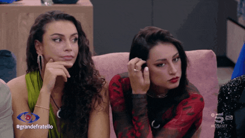 two women are sitting on a couch with the hashtag grandefratello on the screen