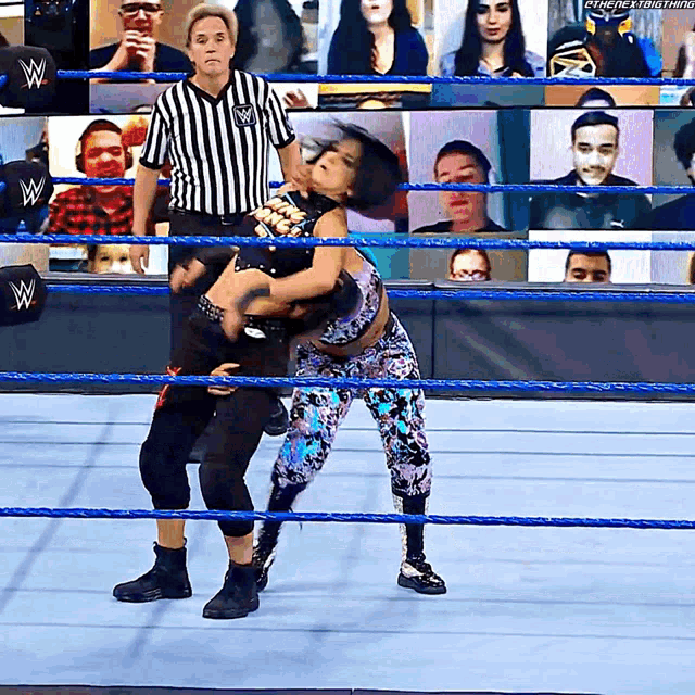 a wrestler is holding another wrestler in a wrestling ring while a referee looks on