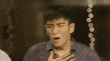 a man in a blue shirt is holding his chest and making a funny face .