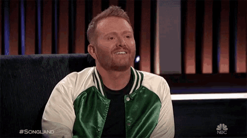 a man wearing a green and white jacket is sitting in front of a screen that says nbc