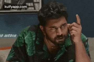 a man with a beard and a green shirt is pointing at the camera .