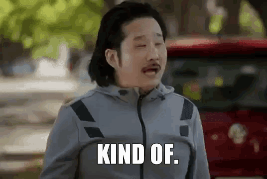 a man with a mustache is standing next to a red car and says kind of .