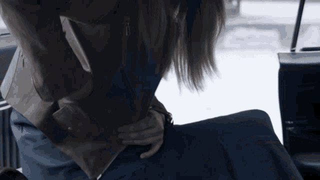 a woman in a brown jacket and blue pants is sitting in the back seat of a car