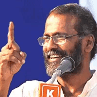 a man with glasses and a beard is speaking into a microphone that has the letter k on it