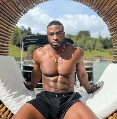 a shirtless man is sitting on a chair with a necklace that says ' jesus ' on it