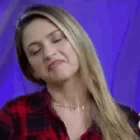 a woman with long blonde hair is wearing a red and black plaid shirt and making a funny face .