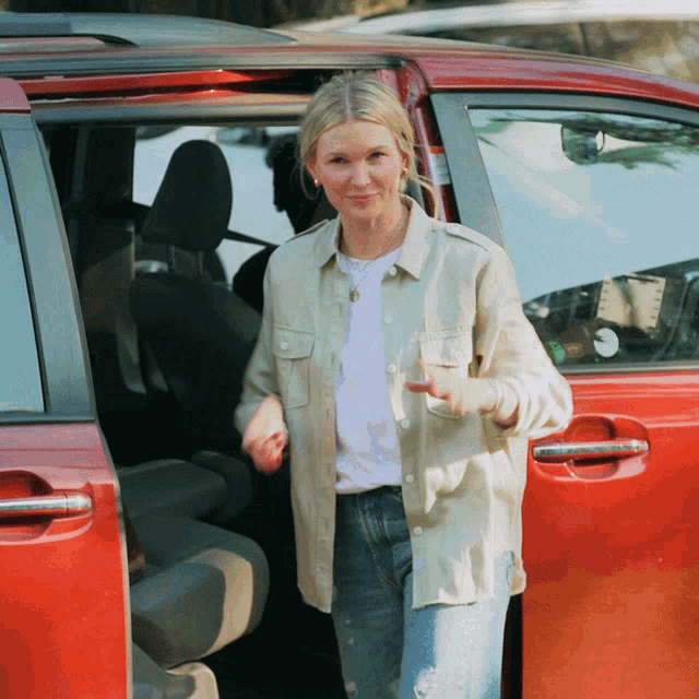 a woman in a tan shirt is getting out of a red van