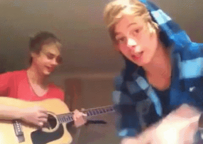 two young men are playing guitars in a room and one of them is wearing a hoodie .