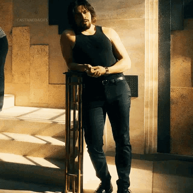 a man in a black tank top leans against a railing in front of a building