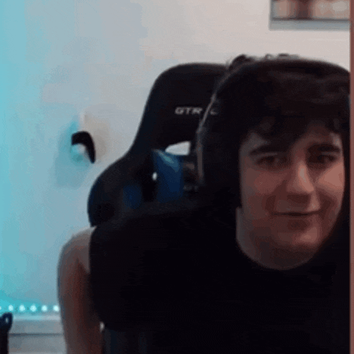 a young man wearing headphones is sitting in a gaming chair and smiling .