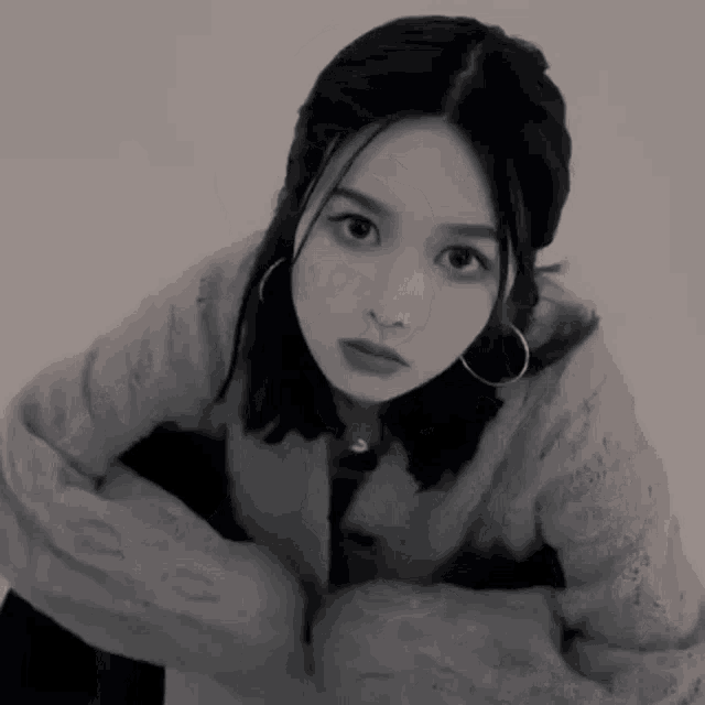 a black and white photo of a woman wearing earrings and a sweater .