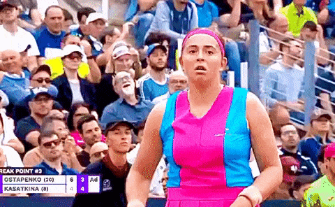 a tennis player in a pink and blue dress is standing in front of a crowd .
