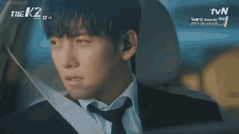 a man in a suit and tie is sitting in the back seat of a car talking to another man .