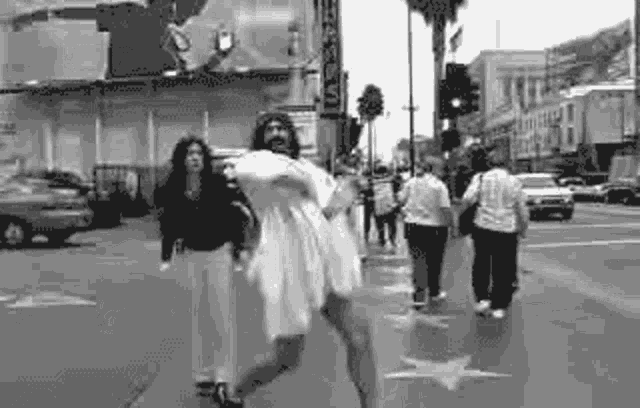a black and white photo of jesus carrying a woman on his shoulders while walking down a street .