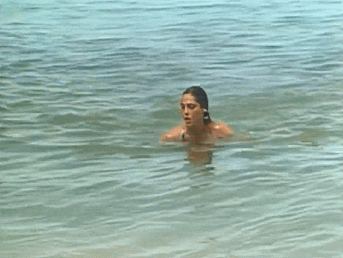 a woman in a black one piece swimsuit is walking out of the water