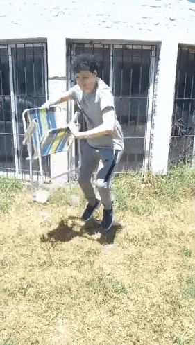 a young man is standing in the grass holding a beach chair .